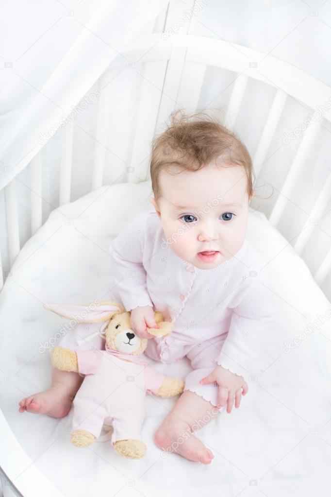 Baby Girl In A White Round Crib With Pink Bunny Toy Stock Photo