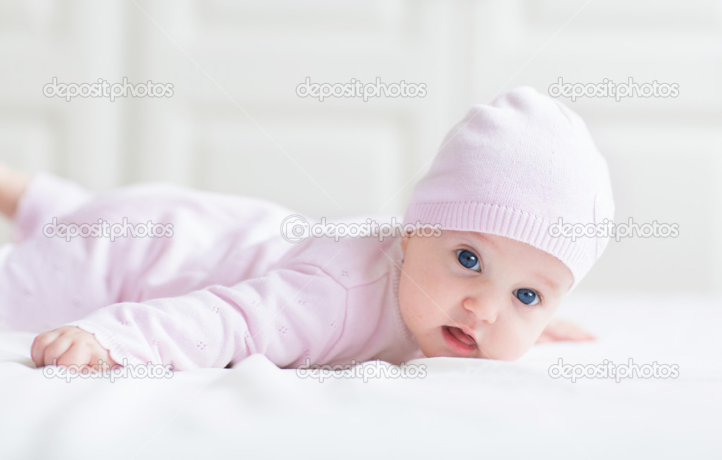 Beautiful baby girl with big blue eyes on a white blanket playing on her tummy