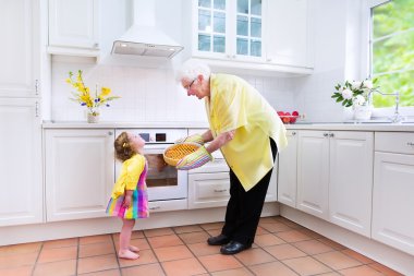 Happy grandmother and little girl baking a pie in a white kitche clipart