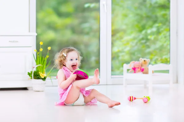 Милая кудрявая девочка играет в бубен в солнечной белой комнате — стоковое фото