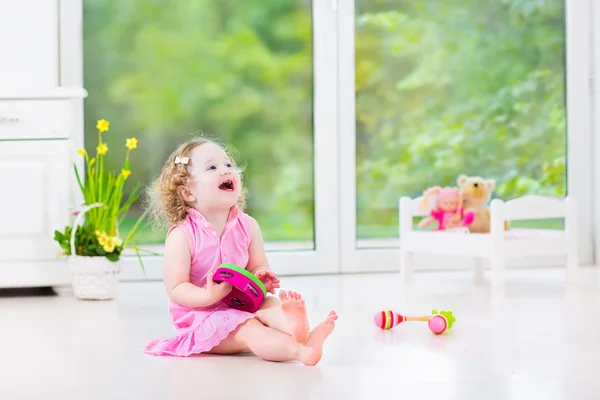 Schattig krullend peuter meisje tamboerijn spelen in een zonnige witte kamer — Stockfoto