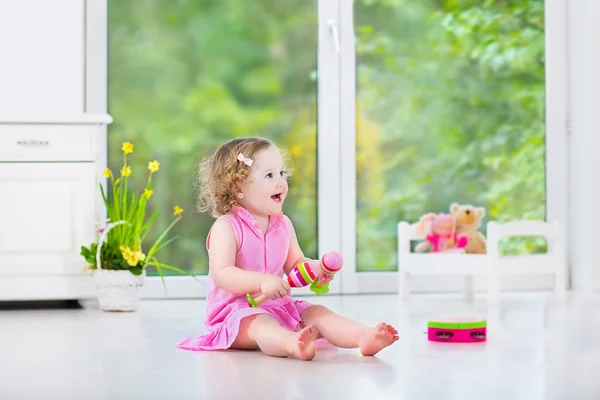 Cute curly toddler girl playing tambourine in a sunny white room — Stock Photo, Image