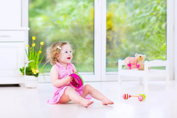 Schattig krullend peuter meisje tamboerijn spelen in een zonnige witte kamer — Stockfoto