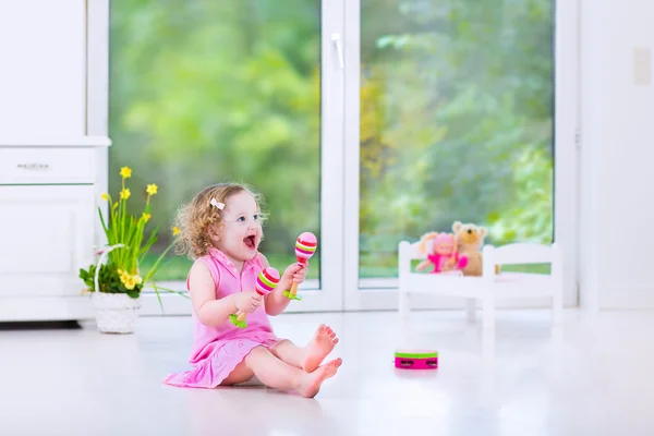 Bonito encaracolado criança menina jogar pandeiro no um ensolarado branco quarto — Fotografia de Stock