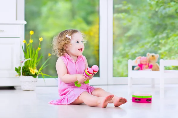 Cute curly toddler girl playing tambourine in a sunny white room — Stock Photo, Image