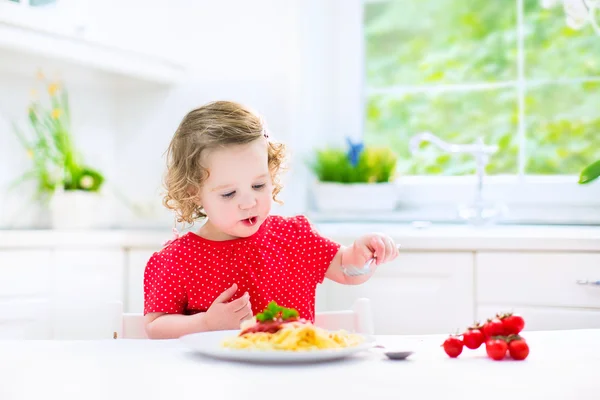 Cute toddler girl eating spaghetti in a white kitchen — Stock Photo, Image