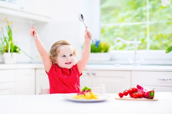 Cute toddler girl eating spaghetti in a white kitchen — Stock Photo, Image