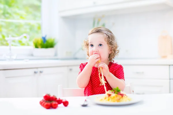 Linda niña comiendo espaguetis en una cocina blanca —  Fotos de Stock