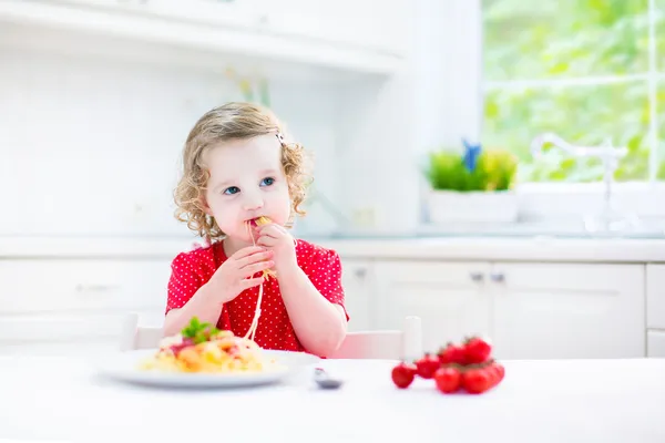 Cute toddler girl eating spaghetti in a white kitchen — Stock Photo, Image