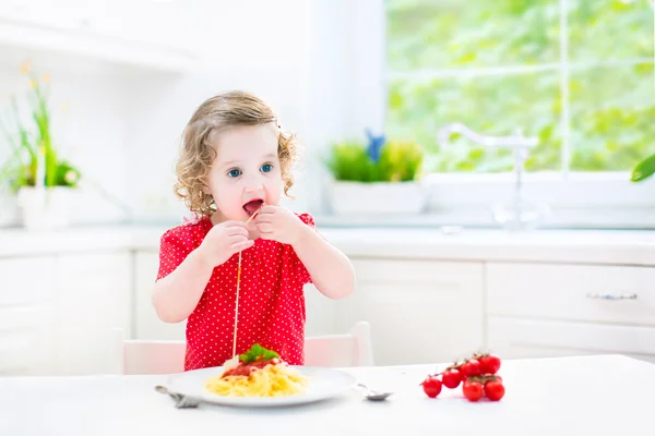 Cute toddler girl eating spaghetti in a white kitchen — Stock Photo, Image