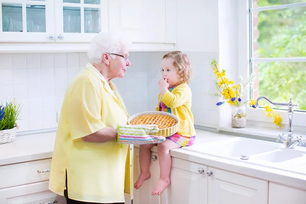 Glückliche Großmutter und kleines Mädchen beim Kuchenbacken in einer weißen Küche — Stockfoto