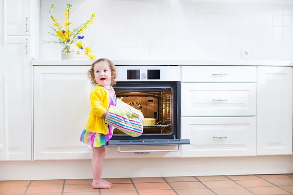 Curly toddler girl in kitchen mittens next to oven with apple pi — Stock Photo, Image