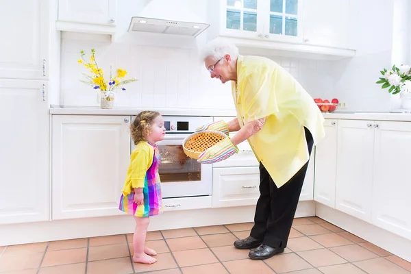Счастливая бабушка и маленькая девочка пекут пирог на белой кухне — стоковое фото