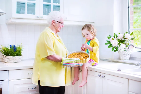 Happy grandmother and little girl baking a pie in a white kitche — Stock Photo, Image