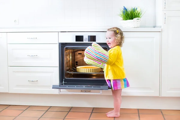 Curly toddler girl in kitchen mittens next to oven with apple pi — Stock Photo, Image