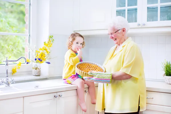 Happy grandmother and little girl baking a pie in a white kitche — Stock Photo, Image
