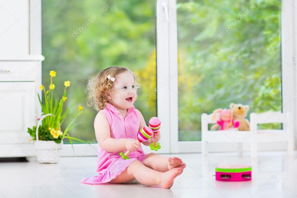 Cute curly toddler girl playing tambourine in a sunny white room