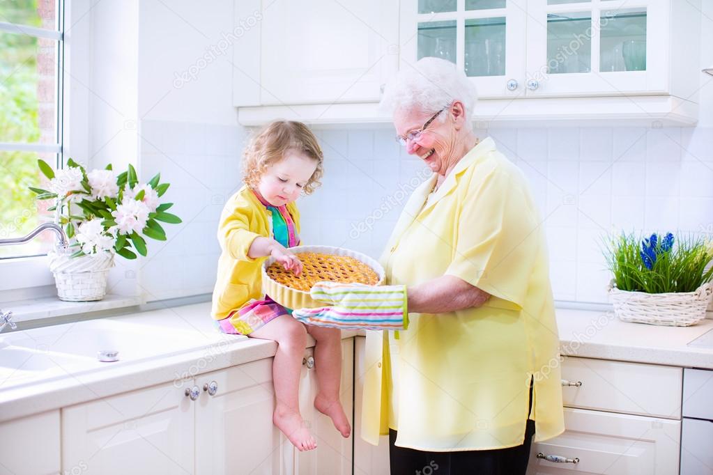 Happy grandmother and little girl baking a pie in a white kitche