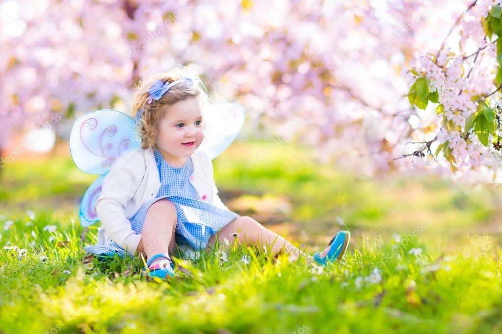 Curly toddler girl in fairy costume playing in fruit garden