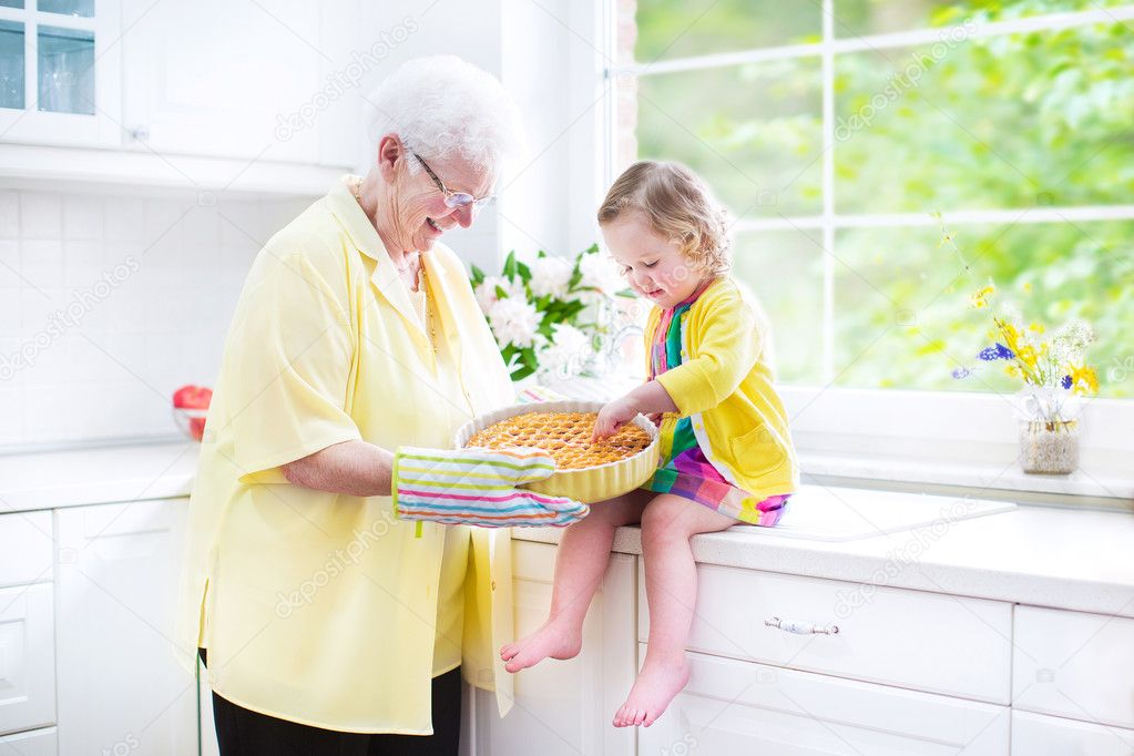 Happy grandmother and little girl baking a pie in a white kitche