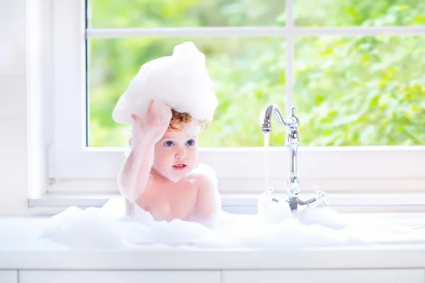 Funny babymeisje spelen met water en schuim in een grote keuken zonde — Stockfoto
