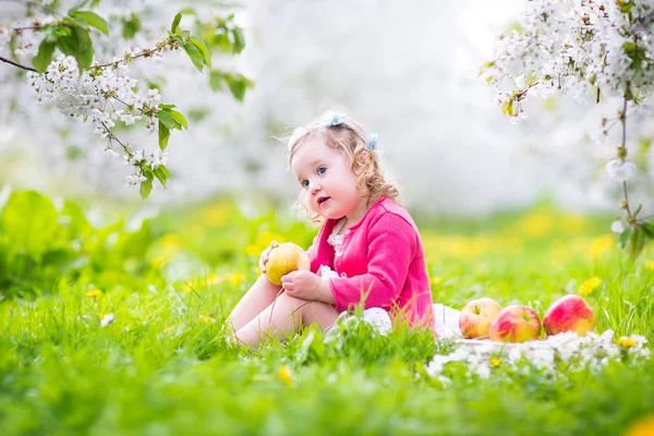 Niedliches Kleinkind isst Apfel in einem blühenden Garten — Stockfoto