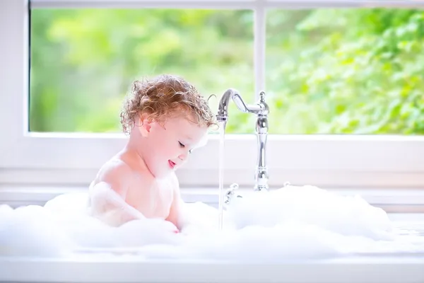 Funny baby girl playing with water and foam in a big kitchen sin — Stock Photo, Image