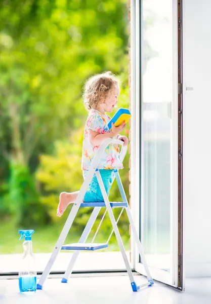 Klein meisje wassen van een venster — Stockfoto