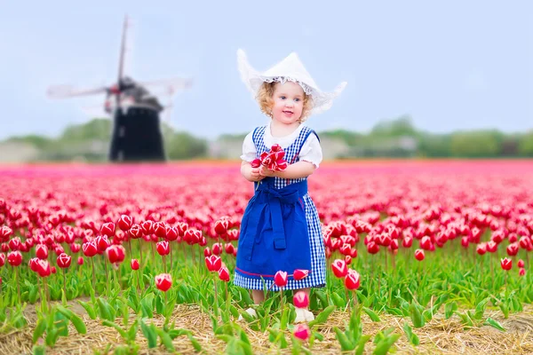 Little girl in a national Dutch costume in tulips field with windmill — Stock Photo, Image