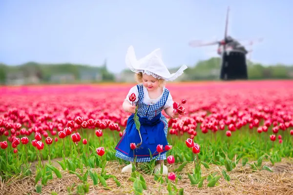 Little girl in a national Dutch costume in tulips field with windmill — Stock Photo, Image