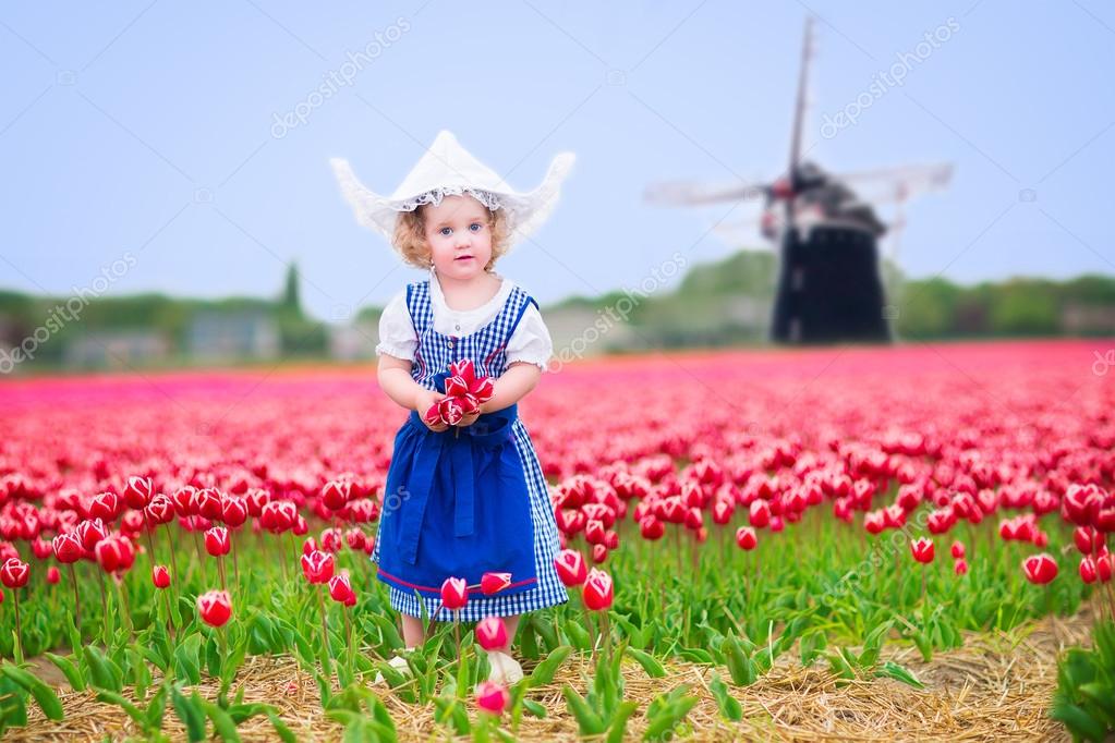 Little girl in a national Dutch costume in tulips field with windmill ...