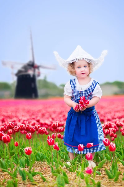 Little girl in a national Dutch costume in tulips field with win — Stock Photo, Image