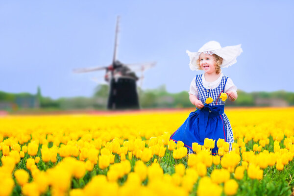Little girl in a national Dutch costume in tulips field with windmill