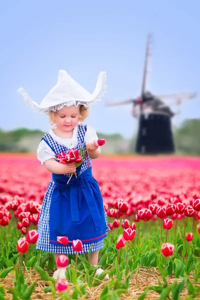 Little girl in a national Dutch costume in tulips field with windmill — Stock Photo, Image