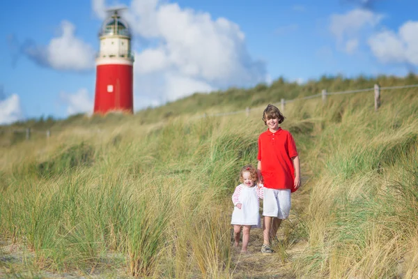 Brother and sister playing on the beach next to a lighthouse — Stock Photo, Image