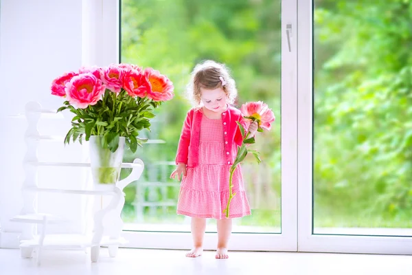 Batole dívka si hraje s Pivoňka květy — Stock fotografie