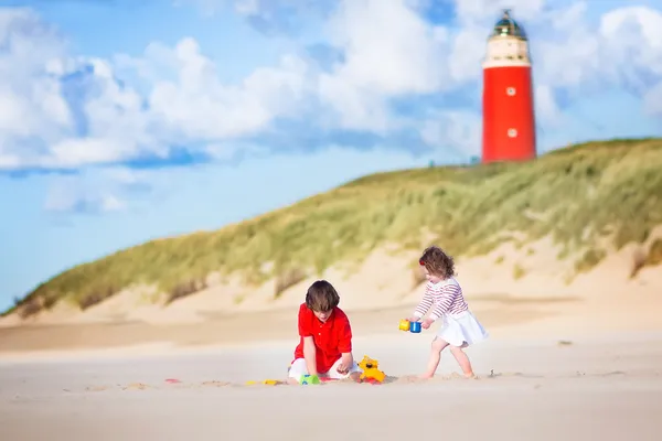 Brother and sister playing on the beach next to a lighthouse — Stock Photo, Image