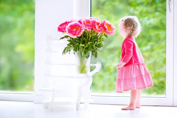 Маленькая девочка играет с пионерскими цветами — стоковое фото