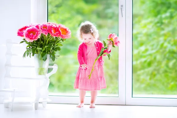 Batole dívka si hraje s Pivoňka květy — Stock fotografie