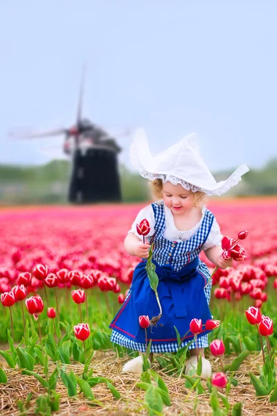 Little girl in a national Dutch costume in tulips field with win — Stock Photo, Image