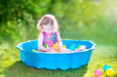 Toddler girl playing wil balls in the garden clipart