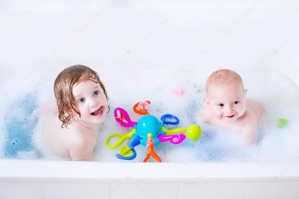 Two little kids playing in a bath tub with toys
