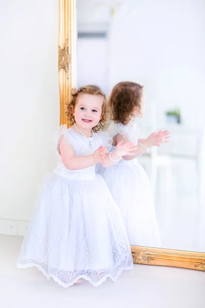 Little girl in a white dress next to a mirror — Stock Photo, Image