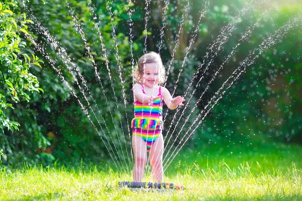 Malá dívka si hraje s zahradní postřikovače — Stock fotografie