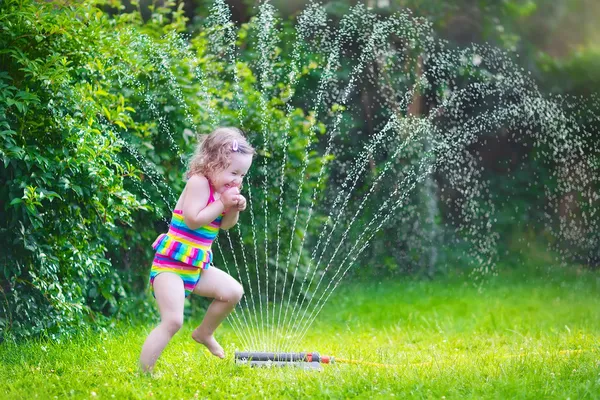 Malá dívka si hraje s zahradní postřikovače — Stock fotografie