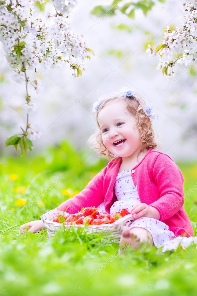 Toddler girl eating strawberry in blooming garden