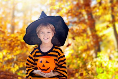 Çocuklar Cadılar Bayramı kostümüyle şeker mi şaka mı oynuyorlar. Banliyöde renkli elbiseli çocuklar şeker kovası ile geziyorlar. Küçük oğlan ve kız balkabağı feneriyle şeker mi şaka mı? Sonbahar tatili eğlencesi.