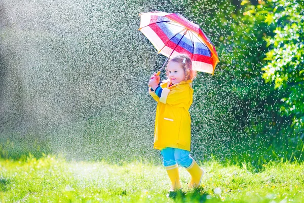 Lustiges Kleinkind mit Regenschirm spielt im Regen — Stockfoto