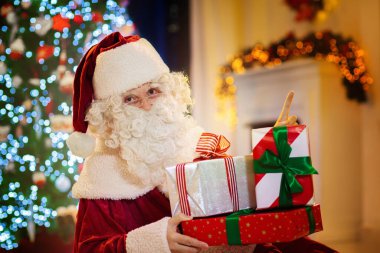 Noel Baba Noel arifesinde hediye getiriyor. Xmas ağacının altında hediyeler. Şömine ve ışıklarla dekore edilmiş oturma odası. Evde kış tatili kutlaması.