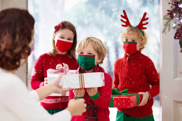 Covid 19流行のクリスマスの日に祖母で子供を持つ家族 玄関のドアで贈り物と顔のマスクの子供たち コロナウイルス隔離中の祖父母との安全なクリスマスのお祝い — ストック写真
